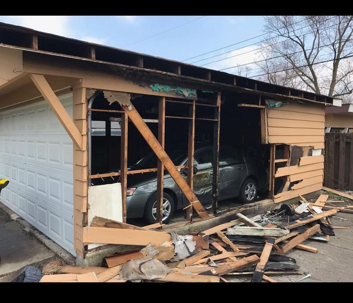 Garage with car inside with one wall damaged by fire.