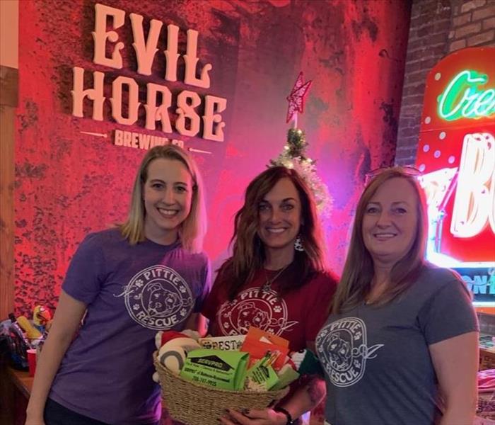 Three female staff members from It's a Pittie Rescue holding a gift basket donated by SERVPRO